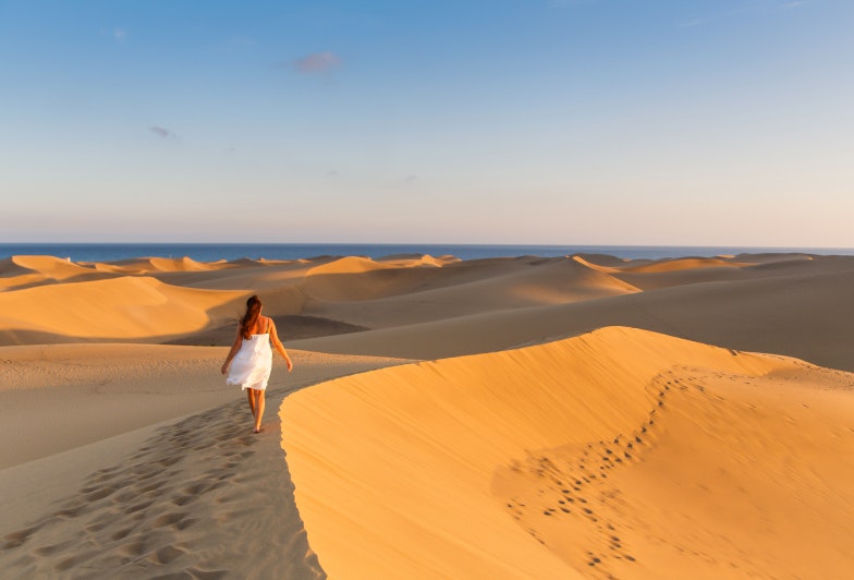 Young beautiful woman walking on the sand wearing white dress at maspalomas dunes bech. Gran Canaria, Spain